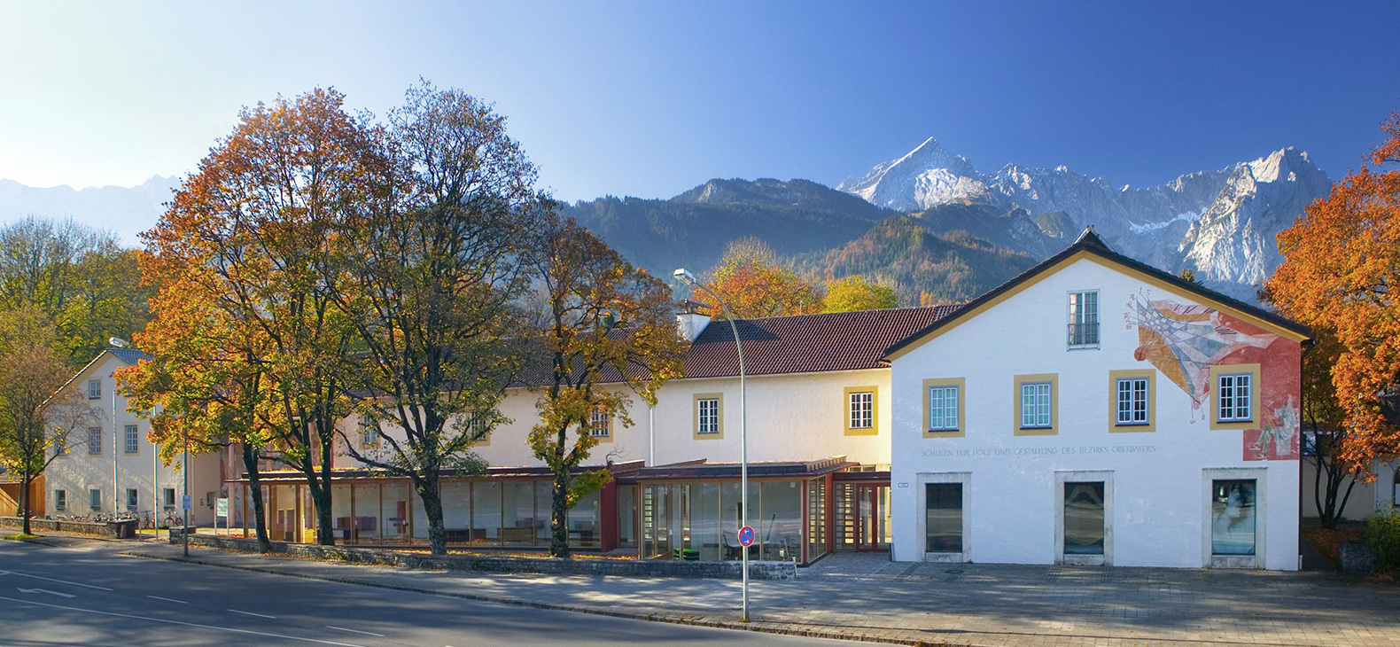 Blick auf die Front des Schulgebäudes an einem sonnigen Wintertag; im Hintergrund die Alpen.