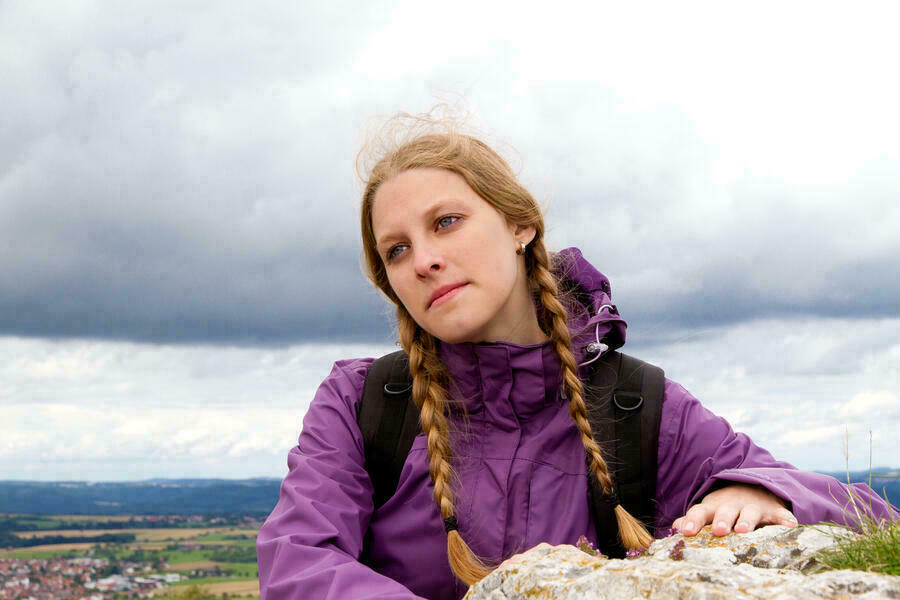 Junge Frau mit 2 geflochtenen Zpfen vor offener Landschaft mit Bergen.