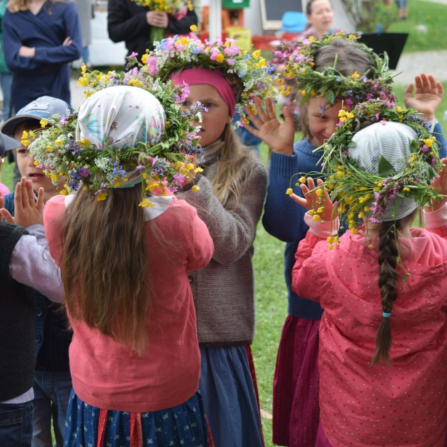 Kinder klatschen gegenseitig die Hände. Auf dem Kopf tragen sie einen selbstgesteckten Blumenkranz.