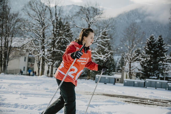 Auf dem Bild ist eine Langläuferin im Schnee mit orangem Trikot zu sehen. 