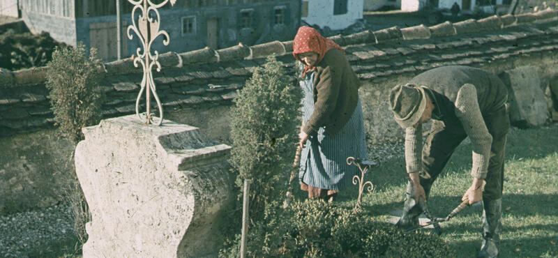Historisches Foto in verblichenen Farben aus den fünfziger Jahren: Eine Frau und ein Mann sind bei der Grabpflege.