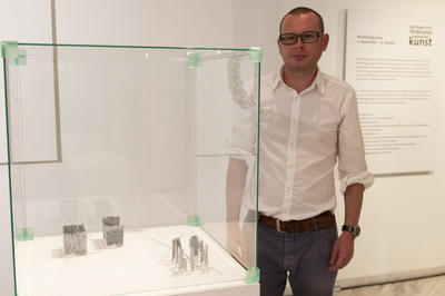 Der Geehrte stehend neben einem Glasschaukasten mit Ausstellungsstücken